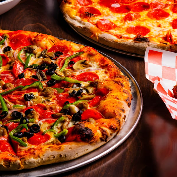Two pizzas, one pepperoni and one supreme with various toppings, on a dark wooden table.