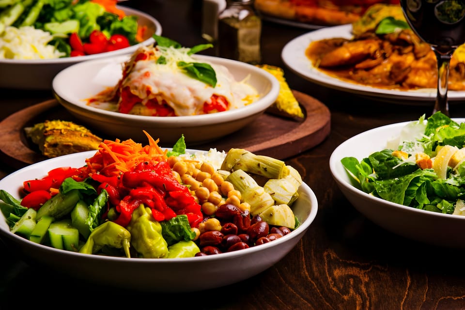 A table laden with various Italian dishes, including salads, lasagna, and a main course.