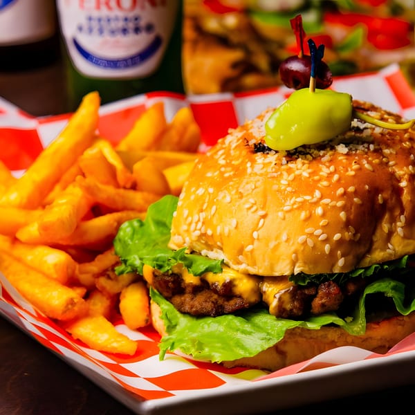 A cheeseburger with lettuce and a pepper on top, served with fries in a red and white checkered basket.