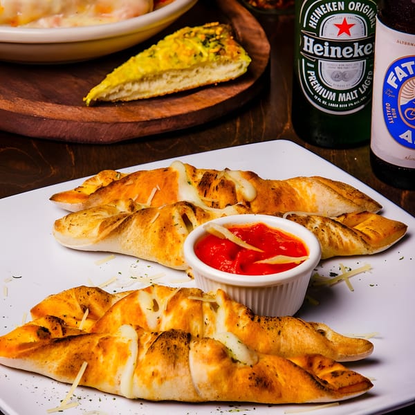 Golden-brown calzones with melted cheese and a side of red sauce, alongside beer bottles.