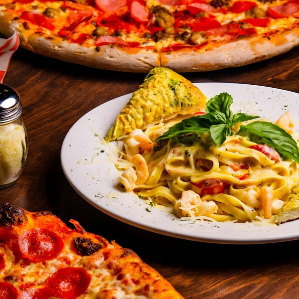 Shrimp fettuccine alfredo with garlic bread, alongside two pizzas on a wooden table.
