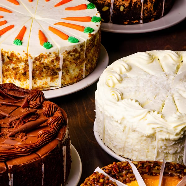 A variety of cakes, including carrot, chocolate, coconut, and pecan, displayed on a table.