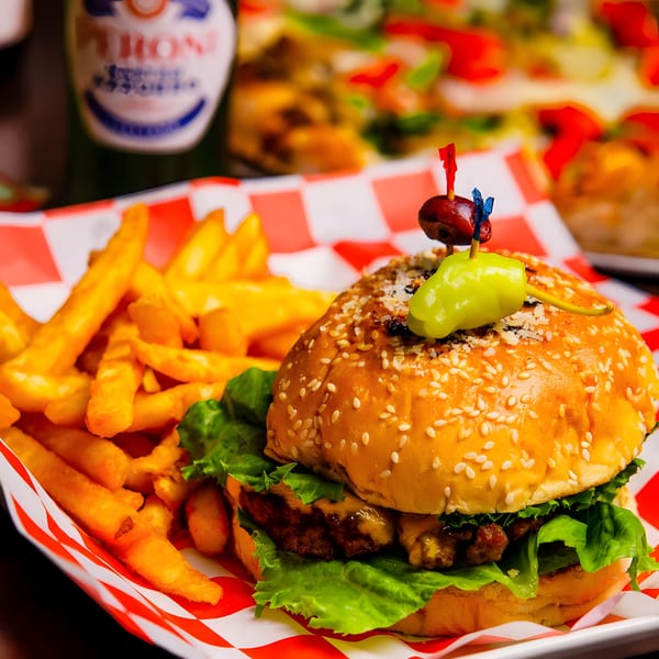 Cheeseburger with lettuce, fries, and a pickled pepper on a red and white checkered paper.